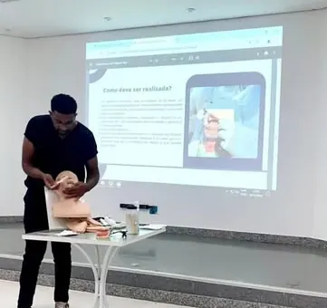 Maylson apresenta uma aula com um modelo de cabeça em uma sala com projetor